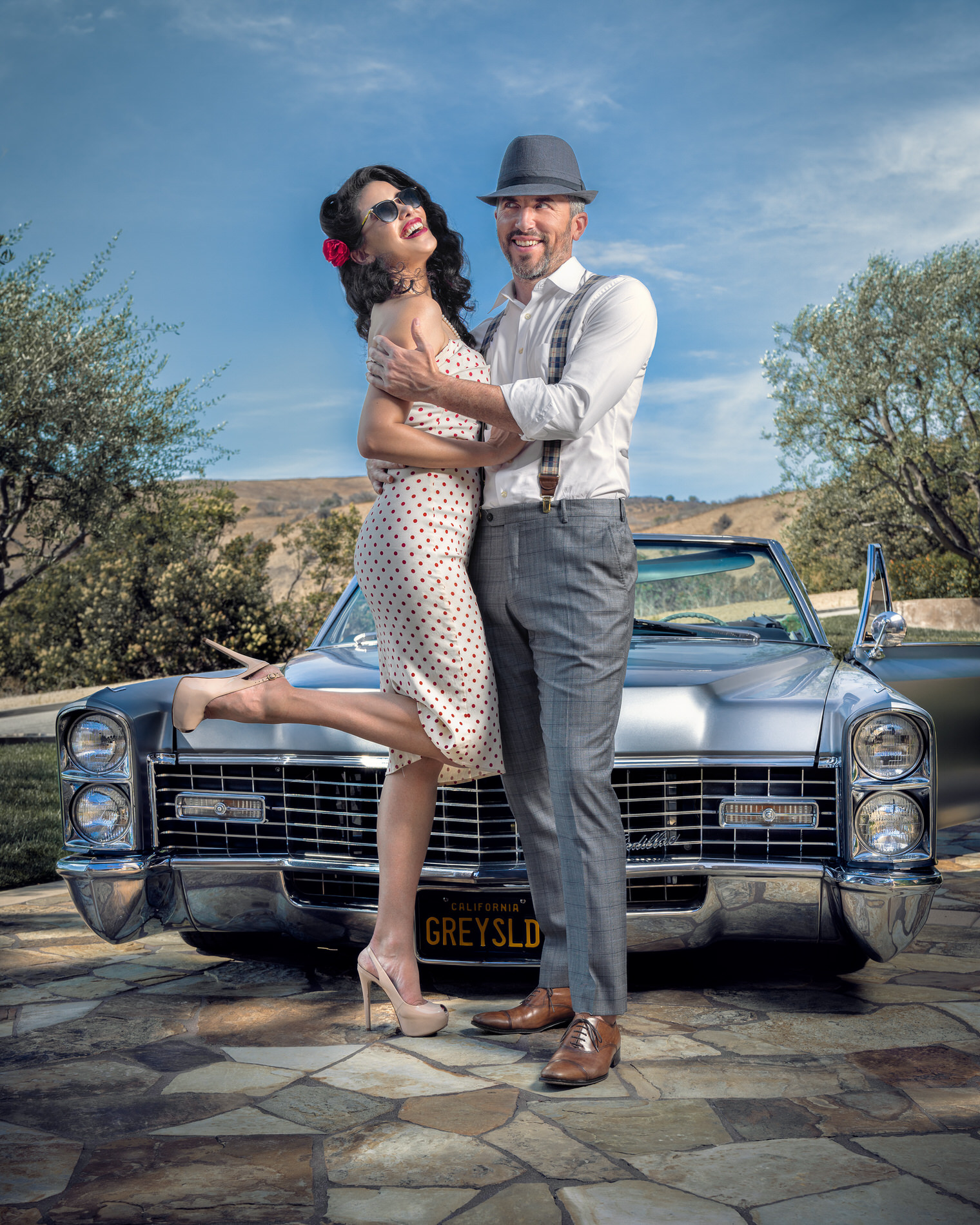 A man holding a woman in front of a old Cadillac.