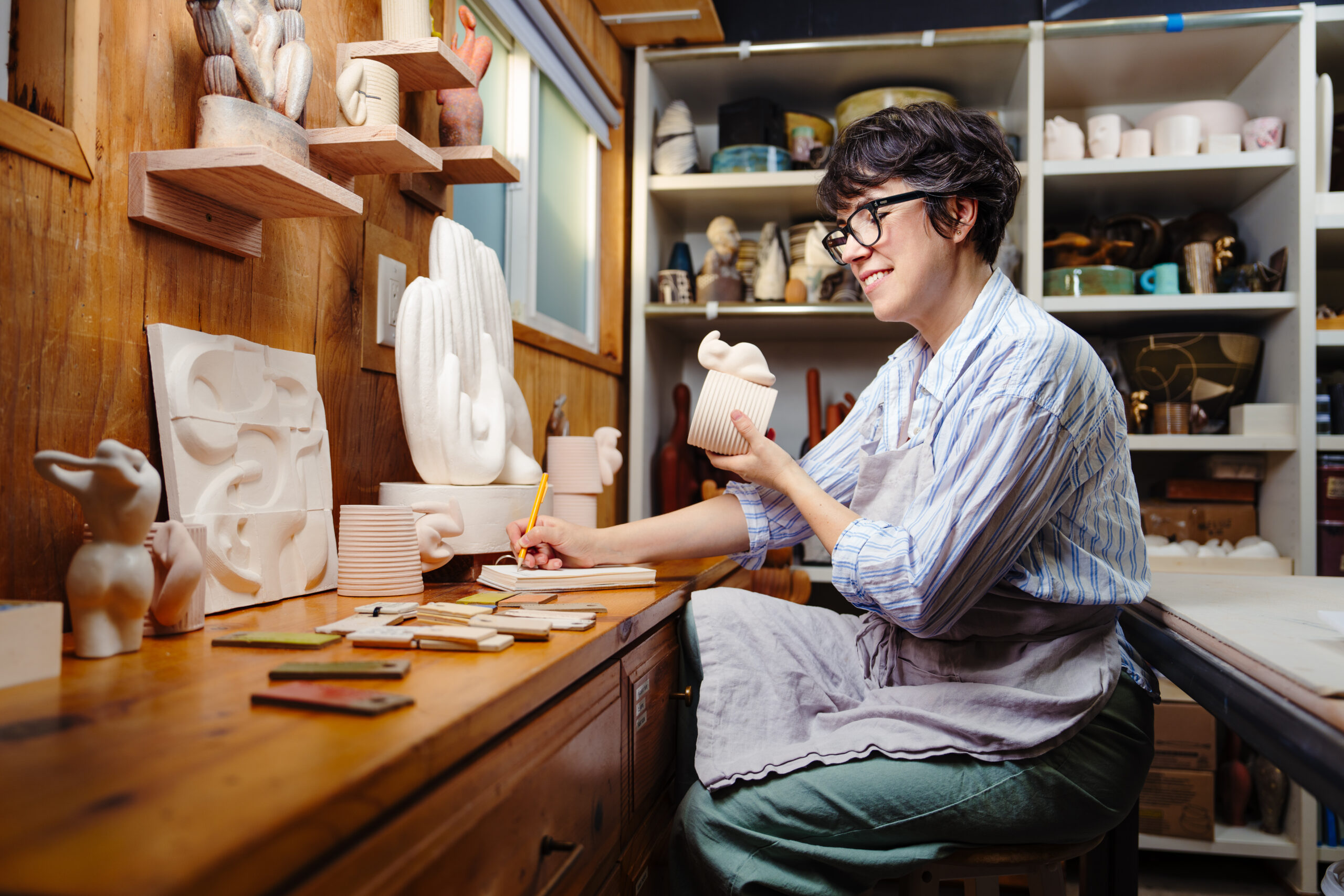A ceramic artist sitting in her studio, inspecting a white ceramic cup